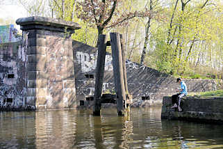 6043 Altes Brückenfundament am Ufer des Tiefstackkanals in Hamburg Billbrook - ein Angler sitzt am Ufer.