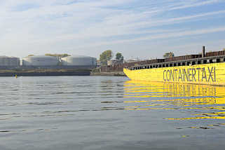 7530 Hafenbecken Petroleumhafen im Hamburger Hafen - ein gelber Leichter mit der Aufschrift Containertaxi liegt an der Spundwand, am Ufer Öltanks.