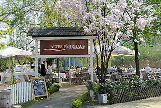 2838 Gartencafé Altes Fährhaus - Tische unter blühenden Krischbäumen.