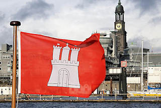 0556  Die Flagge der Hansestadt Hamburg weht im  Wind - im Hintergrund der Turm des Hamburger Wahrzeichens, die St. Michaeliskirche / Michel.