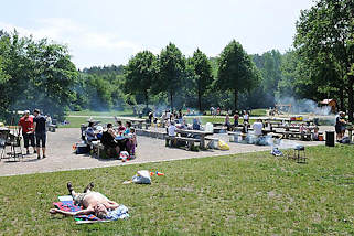 4230 Grillplatz Sandkuhle in Hamburg Rissen - der Platz ist gut besucht - Rauch steigt von den Grills auf; Menschen essen an den Tischen, andere sonnen sich auf der Wiese.