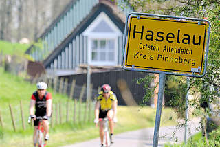 1147 Ortschild Haselau, Ortsteil Altendeich - Kreis Pinneberg; Radfahrer auf der Deichstrasse - Wohnhäuser mit Reet gedeckt.