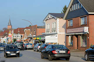 4097 Einzelhäuser, Geschäfte - dichter Strassenverkehr auf der Kieler Strasse in Quickborn; im Hintergrund der Kirchturm der Marienkirche.