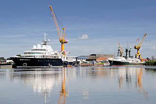 8747 Werftanlagen an der Stör in Wewelsfleet - Schiffe liegen am Ausrüstungskai - Werftkräne stehen am Ufer.