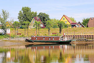 8756 Blick von der Stör auf Wewelsfleet - ein Hausboot liegt bei Niedrigwasser im Schlick - hinter dem Deich Häuser des Dorfes.